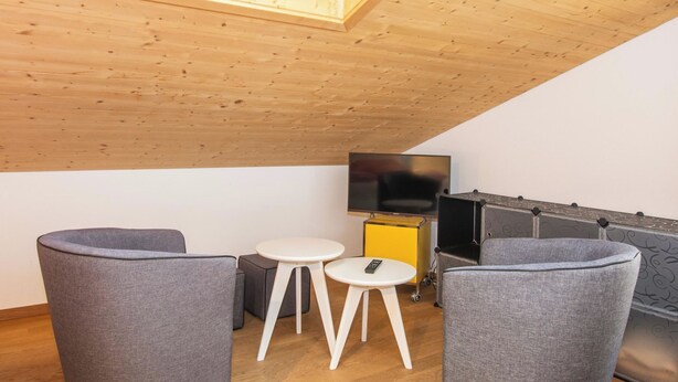 A modern living room with a wooden ceiling, a flat-screen TV, grey upholstered chairs, and a small white table. - Studio Zentrum OG Appartement/Fewo, Dusche, WC, 1 Schlafraum Studio by Interhome (Adelboden)