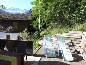 A wooden deck with lounge chairs, a table, and a view of mountains.