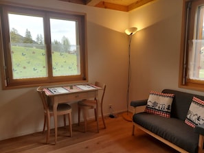 Ein Zimmer mit Schreibtisch aus Holz, zwei Stühlen, einer Couch und einer Stehlampe.