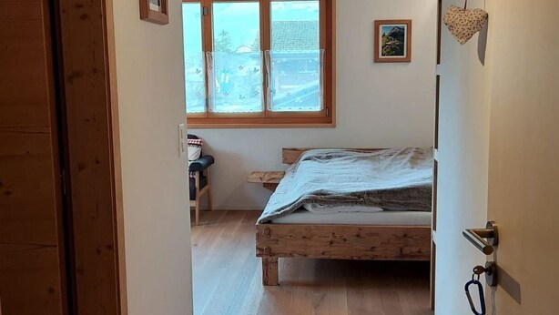 Ein Schlafzimmer mit Holzboden, einem Bett, einem Fenster und einer Tür.