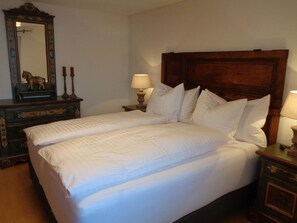 A double bed with white linens, a wooden headboard, two bedside tables with lamps, and a mirror with a decorative horse figure. - Juwel Appartement/Fewo, Dusche, WC, 2 Schlafräume 3-Zimmerwohnung by Interhome (Adelboden)