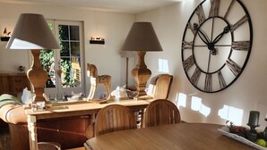 Ein Essbereich mit einem Holztisch, Stühlen und zwei Lampen. Eine große Wanduhr ist zu sehen.