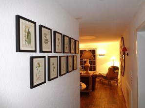 Ein Flur mit gerahmten Pflanzenbildern an der Wand, einer Lampe und einem Sessel.
