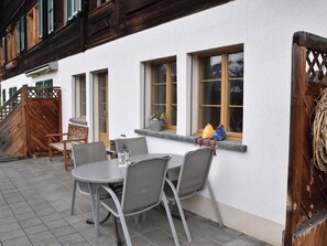 Un patio al aire libre con una mesa redonda y sillas, una escalera de madera y un edificio blanco con ventanas.