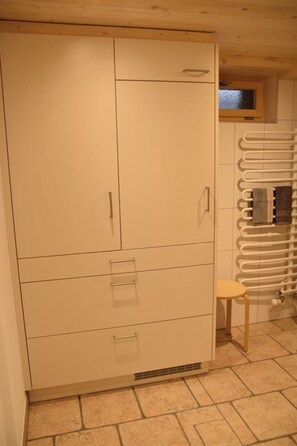 Una habitación con un armario blanco grande, un taburete pequeño y un radiador.