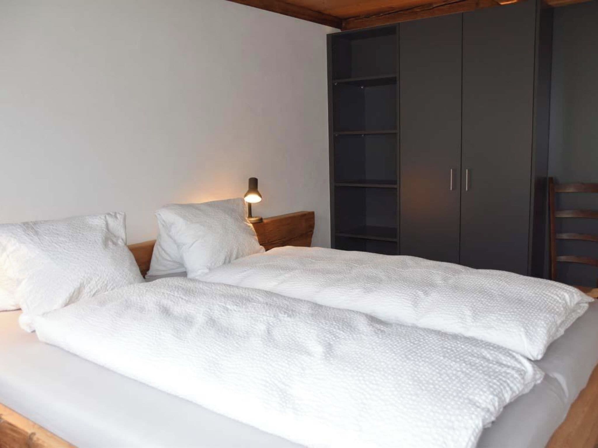 Ein Bett mit weißer Bettwäsche, eine Nachttischlampe und ein Kleiderschrank mit mehreren Türen.
