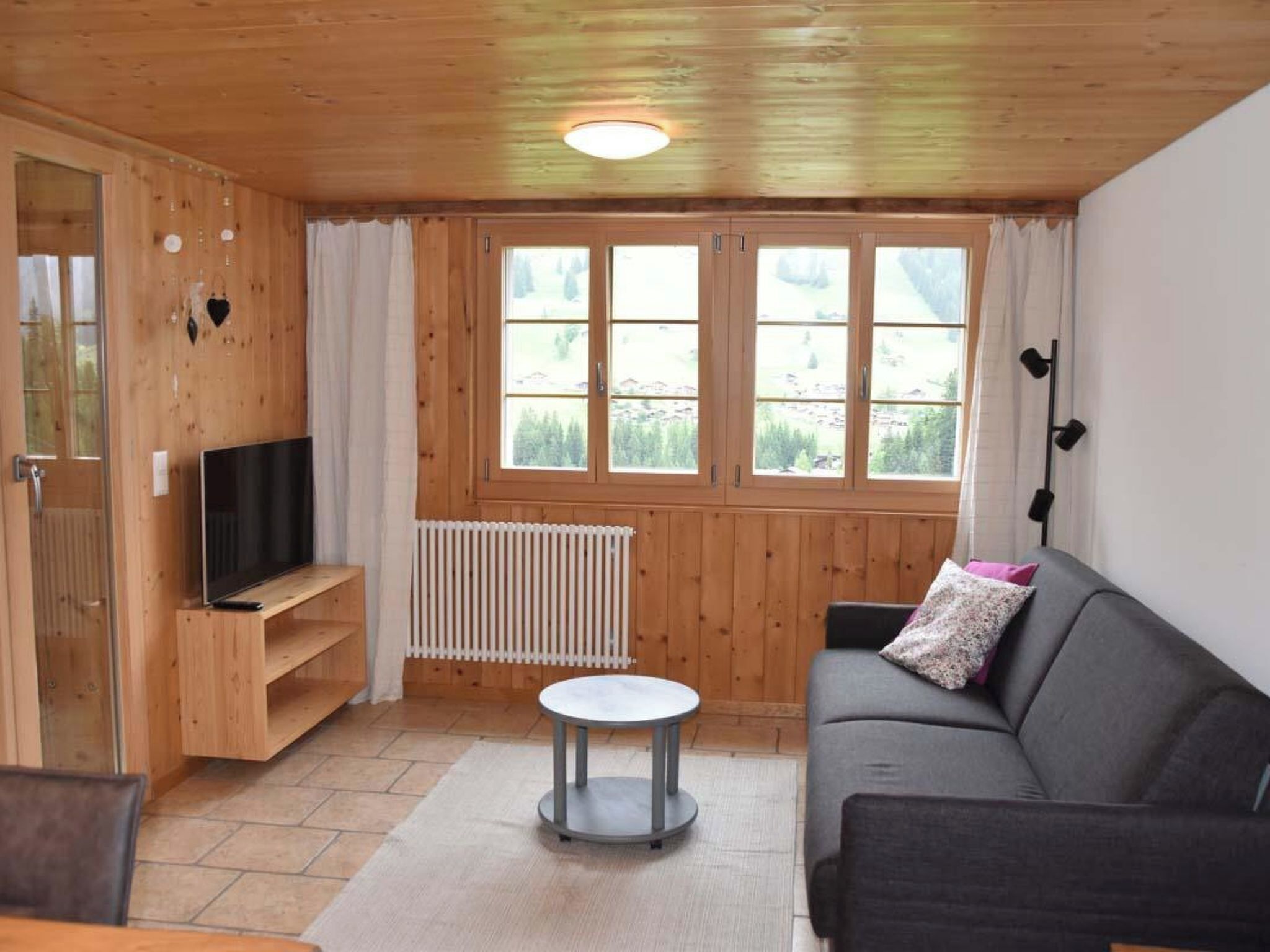 Un salon chaleureux avec un plancher en bois, un canapé noir, une petite table ronde et un téléviseur posé sur un meuble en bois.