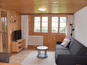 A cozy living room with a wooden floor, a black sofa, a small round table, and a TV on a wooden stand. - Gästehaus Alpengruss Appartement/Fewo, Bad, WC, 1 Schlafraum by Interhome (Adelboden)