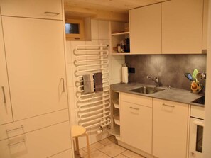 Cocina compacta con horno integrado, un lavamanos y un taburete pequeño.