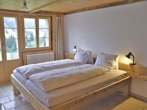A bed with white linens in a room with wooden beams and a view of trees through large windows. - Gästehaus Alpengruss Appartement/Fewo, Bad, WC, 1 Schlafraum by Interhome (Adelboden)