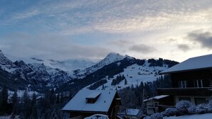 Eine verschneite Berglandschaft mit einem Skigebiet, Chalets und einem Auto im Vordergrund.