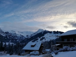 A snow-covered mountain landscape with a ski resort, cabins, and a car parked in the foreground. - Gruebi - Haus Baldrian Appartement/Fewo, Bad, WC, 2 Schlafräume 3-Zimmerwohnung by Interhome (Adelboden)