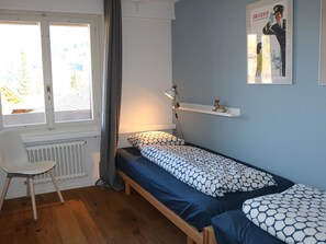 A small, single-bed room with a window, a radiator, a desk, and a chair. - Gruebi - Haus Baldrian Appartement/Fewo, Bad, WC, 2 Schlafräume 3-Zimmerwohnung by Interhome (Adelboden)