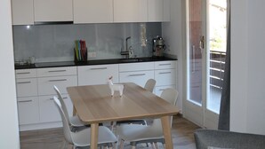 Eine moderne Küche mit weißen Schränken, einem Holzes Esstisch und einer Glastür, die auf einen Balkon führt.
