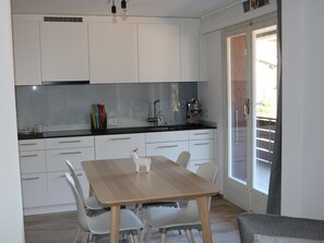 A modern kitchen with white cabinets, a wooden dining table, and a glass door leading to a balcony. - Gruebi - Haus Baldrian Appartement/Fewo, Bad, WC, 2 Schlafräume 3-Zimmerwohnung by Interhome (Adelboden)