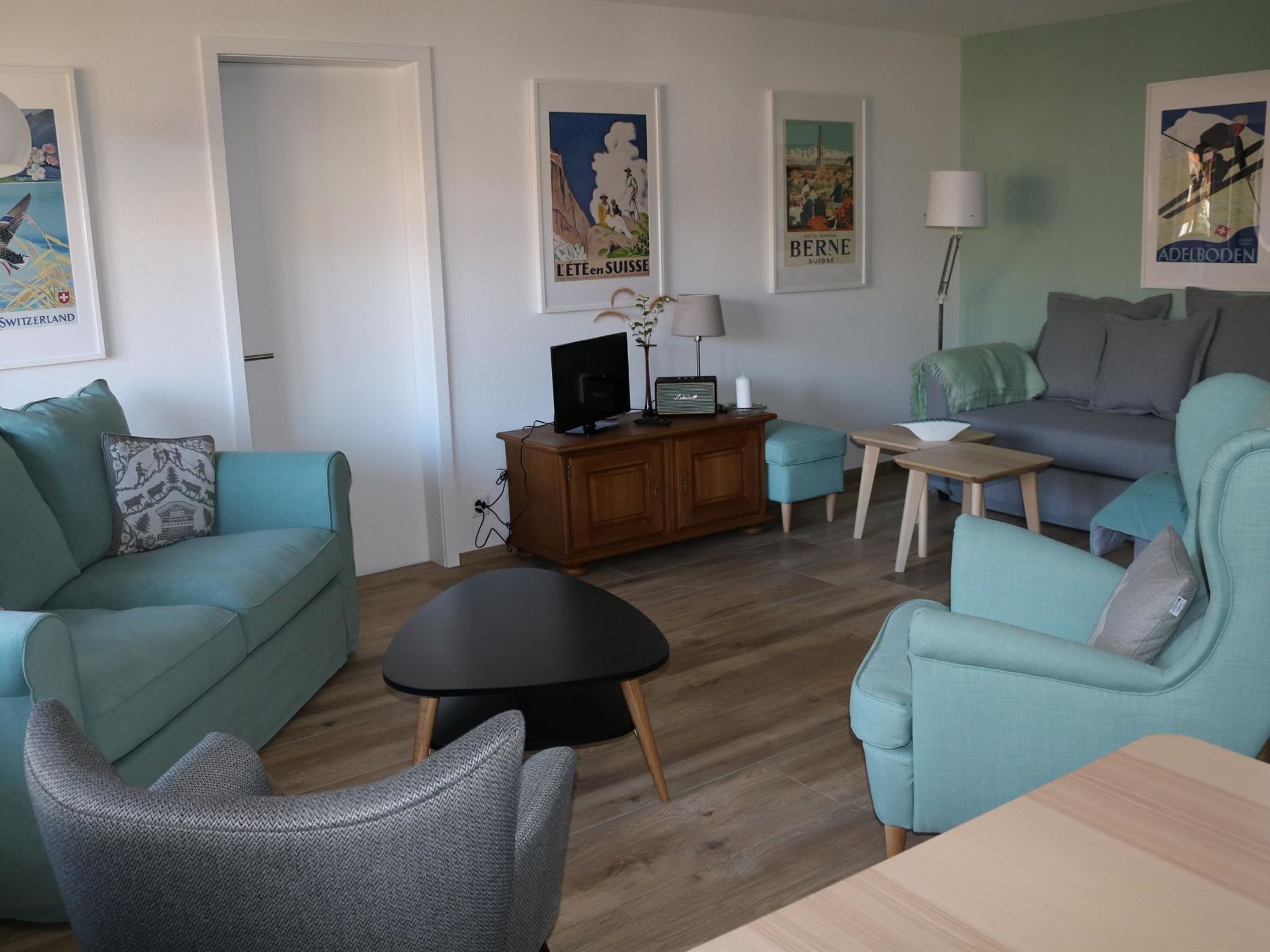 Een moderne woonkamer met blauwgroene banken, een zwarte salontafel en een houten kast.