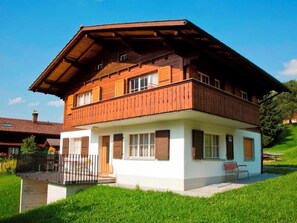A two-story wooden house with a balcony, a fenced yard, and a bench. - Dayuma Parterre Appartement/Fewo, Bad, WC, 2 Schlafräume by Interhome (Adelboden)