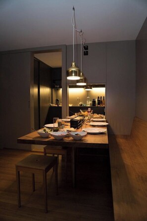 A modern kitchen with a long wooden table, hanging pendant lights, and a visible door leading to another room. - Dayuma Parterre Appartement/Fewo, Bad, WC, 2 Schlafräume by Interhome (Adelboden)