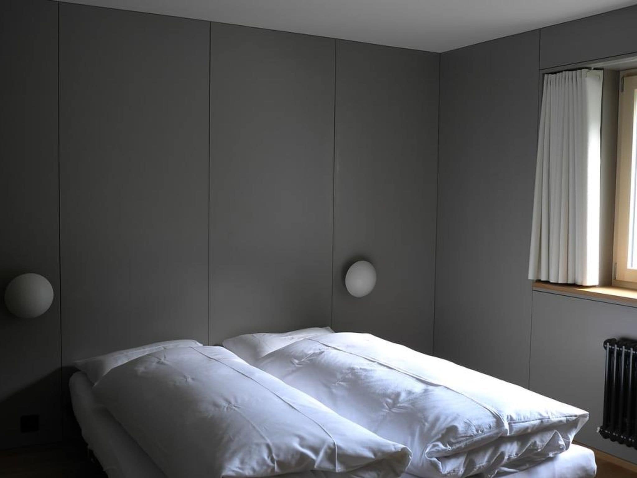 A bedroom with a bed, a window with curtains, and a radiator.