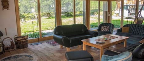 A spacious living area with large windows, a black leather sofa, a wooden coffee table, and a view of the outdoors.