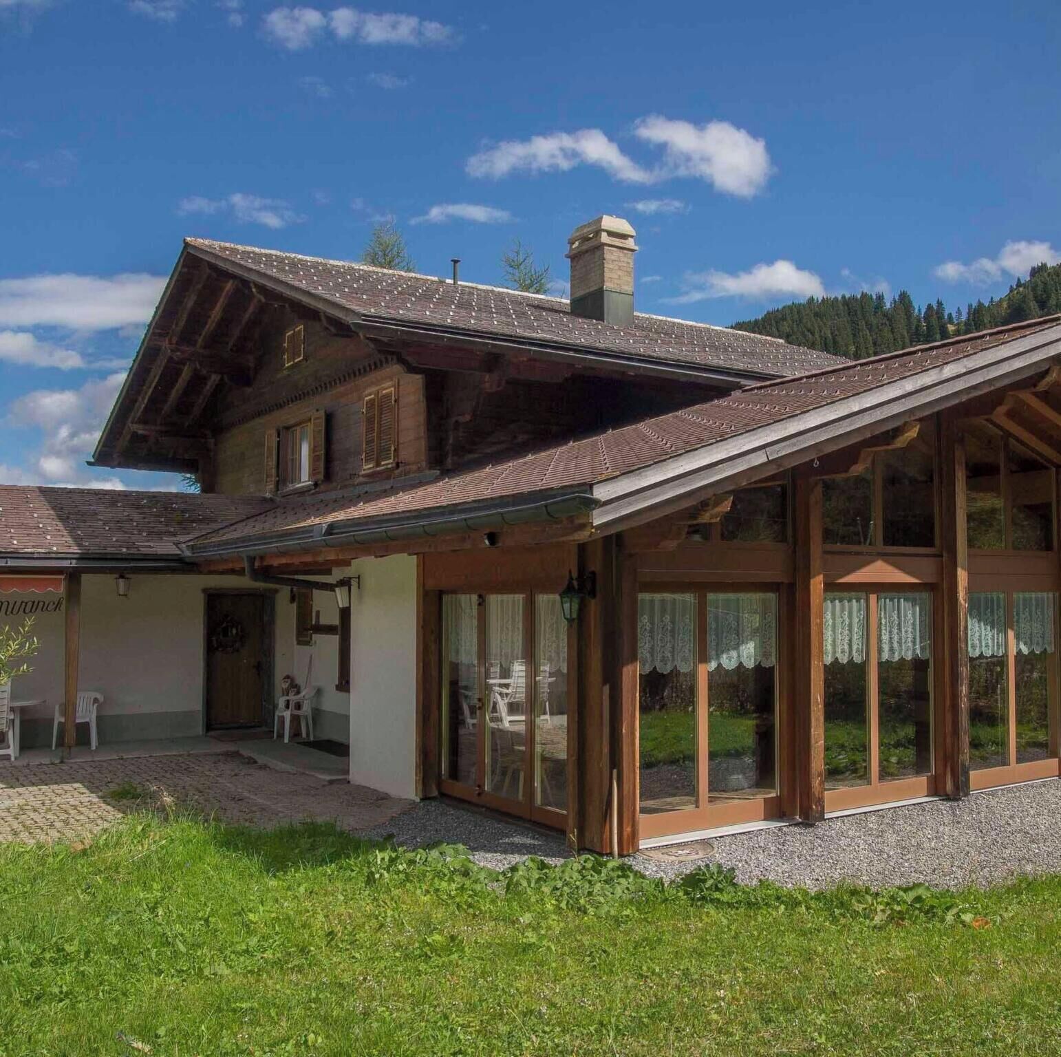 Ein traditionelles Chalet mit geneigtem Dach, Holzfassade und großen Glasüren.