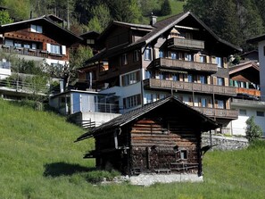 A traditional wooden chalet with a stone foundation, surrounded by modern multi-story buildings with balconies. - Waldrand Appartement/Fewo, Bad, WC, 2 Schlafräume 3-Zimmerwohnung by Interhome (Adelboden)