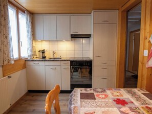Eine kompakte Küche mit Backofen, einem Esstisch mit gemustertem Tischläufer und einem Fenster mit Vorhängen.