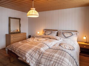 A bedroom with a wooden ceiling, a bed with a plaid bedspread, two bedside lamps, and a dresser with a mirror. - Waldrand Appartement/Fewo, Bad, WC, 2 Schlafräume 3-Zimmerwohnung by Interhome (Adelboden)