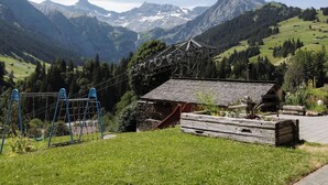 Eine Berglandschaft mit einem kleinen Gebäude, einem Spielplatz und einem Holzzaun.