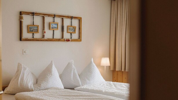 Ein Hotelzimmer mit zwei Betten, einem Holzkopfteil, einem an der Wand befestigten Bilderrahmen und einer Nachttischlampe.