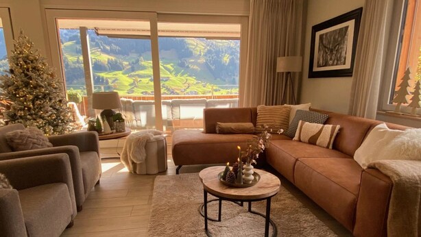 Ein gemütliches Wohnzimmer mit braunem Sofa, Sesseln, einem Couchtisch und einem Weihnachtsbaum.
