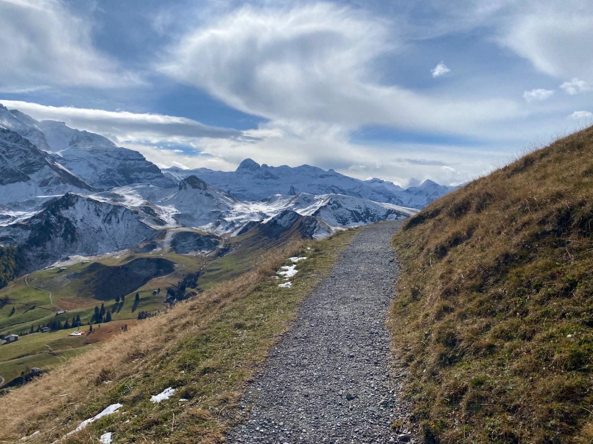 Un sendero de grava que serpentea por una zona montañosa con picos nevados al fondo.