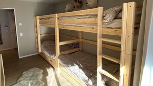 Ein Schlafraum mit Etagenbetten, einer grauen Wand, einer weißen Tür und einem hellerfarbenen Teppich.