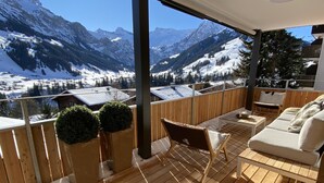 Eine Holzterrasse mit einer Couch und Stühlen, mit Blick auf eine verschneite Berglandschaft.