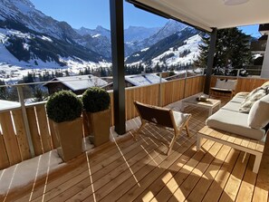 Eine Holzterrasse mit einer Couch und Stühlen, mit Blick auf eine verschneite Berglandschaft.