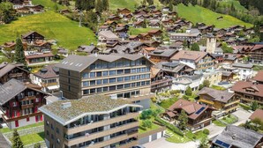 Ein modernes Gebäude mit flachem Dach und mehreren Balkonen, umgeben von traditionellen Häusern mit schrägen Dächern.