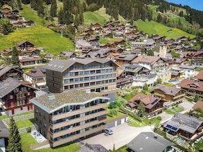Ein modernes Gebäude mit flachem Dach und mehreren Balkonen, umgeben von traditionellen Häusern mit schrägen Dächern.