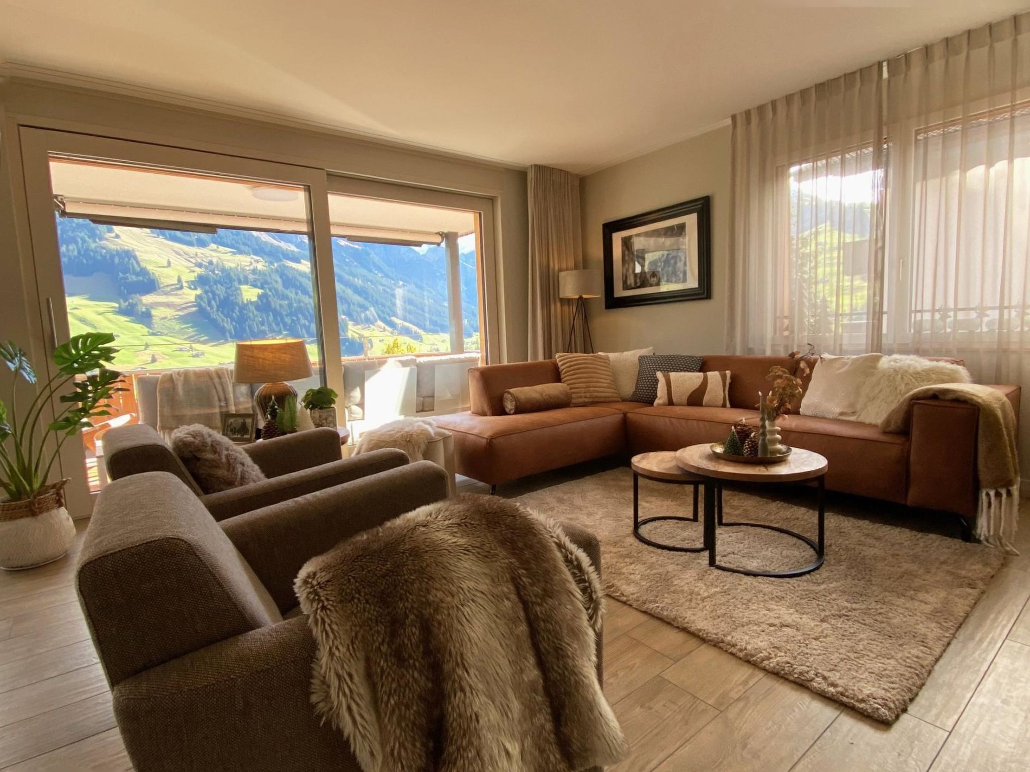 Un salon comprenant un canapé, des fauteuils, une table basse et offrant une vue sur un paysage montagneux grâce à de grandes fenêtres.