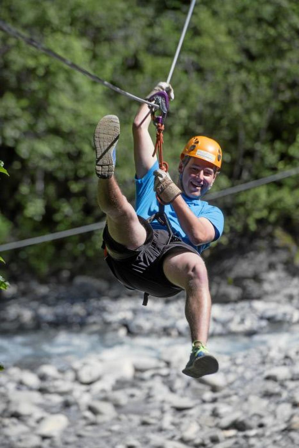 Eine Person bei einer Outdoor-Aktivität, mit Helm und Klettergeschirr, ein Seil und ein Sicherungssystem sind sichtbar.