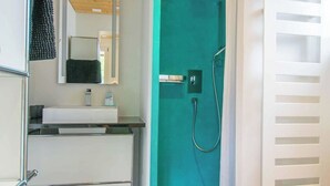 Et moderne badeværelse med bruseniche, toilet og vaskebord med spejl.