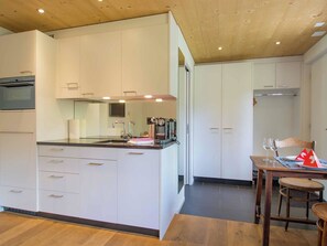 Eine moderne Küche mit weißen Schränken, einem eingebauten Backofen und einem Essbereich mit einem Holztisch und Stühlen.