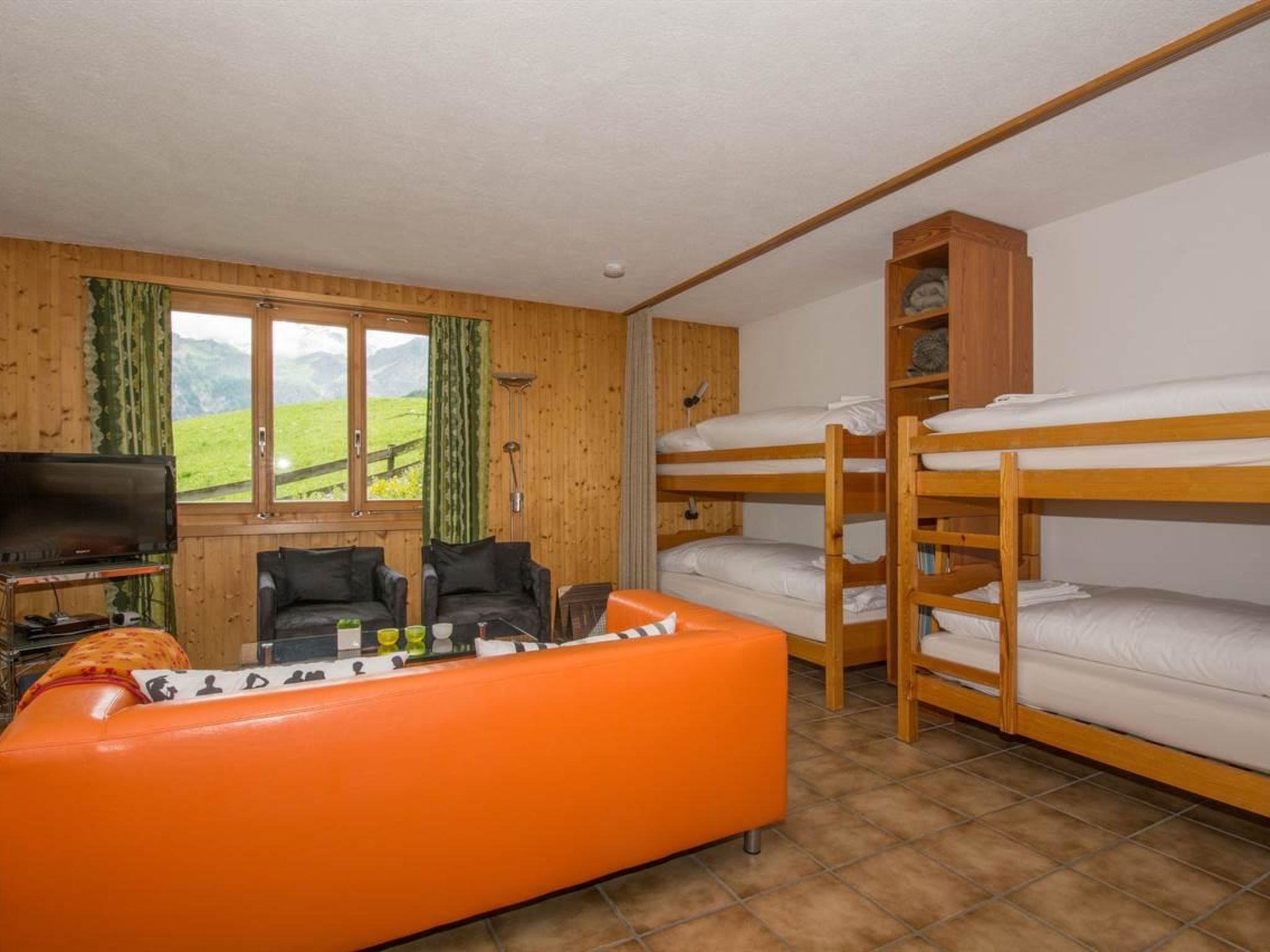 Une chambre avec des lits superposés, un canapé, une télévision et une fenêtre donnant sur un paysage verdoyant.