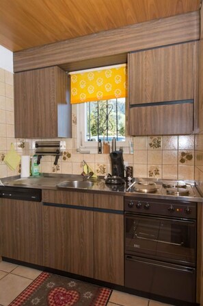 Une cuisine avec des meubles de rangement en bois, un four encastré, une machine à café et une fenêtre ornée d’un rideau à motifs jaunes.