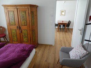 Ett rum med en säng, en garderob, ett matbord med stolar och en liten fåtölj.