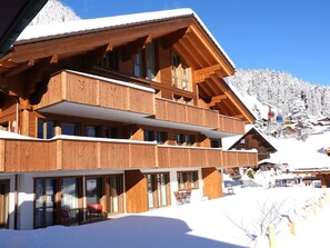 Una cabaña de madera de varios pisos con balcones, ventanas amplias y un paisaje montañoso nevado.