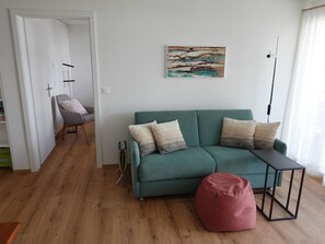 Ett vardagsrum med en turkos soffa, en röd sittpuff, en tavla på väggen och ett litet bord.
