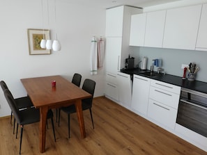 A modern kitchen with white cabinets, a wooden dining table, and black chairs. - Am Bellevuegässli Appartement/Fewo, Bad, WC, 1 Schlafraum 2,5 - Zimmerwohnung by Interhome (Adelboden)