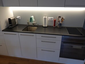 Una cocina moderna con un lavamanos de acero inoxidable, una cafetera, un dispensador de toallas de papel y un especiero.