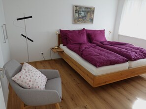 A bedroom with a wooden bed, a grey armchair, and a white pillow. - Am Bellevuegässli Appartement/Fewo, Bad, WC, 1 Schlafraum 2,5 - Zimmerwohnung by Interhome (Adelboden)