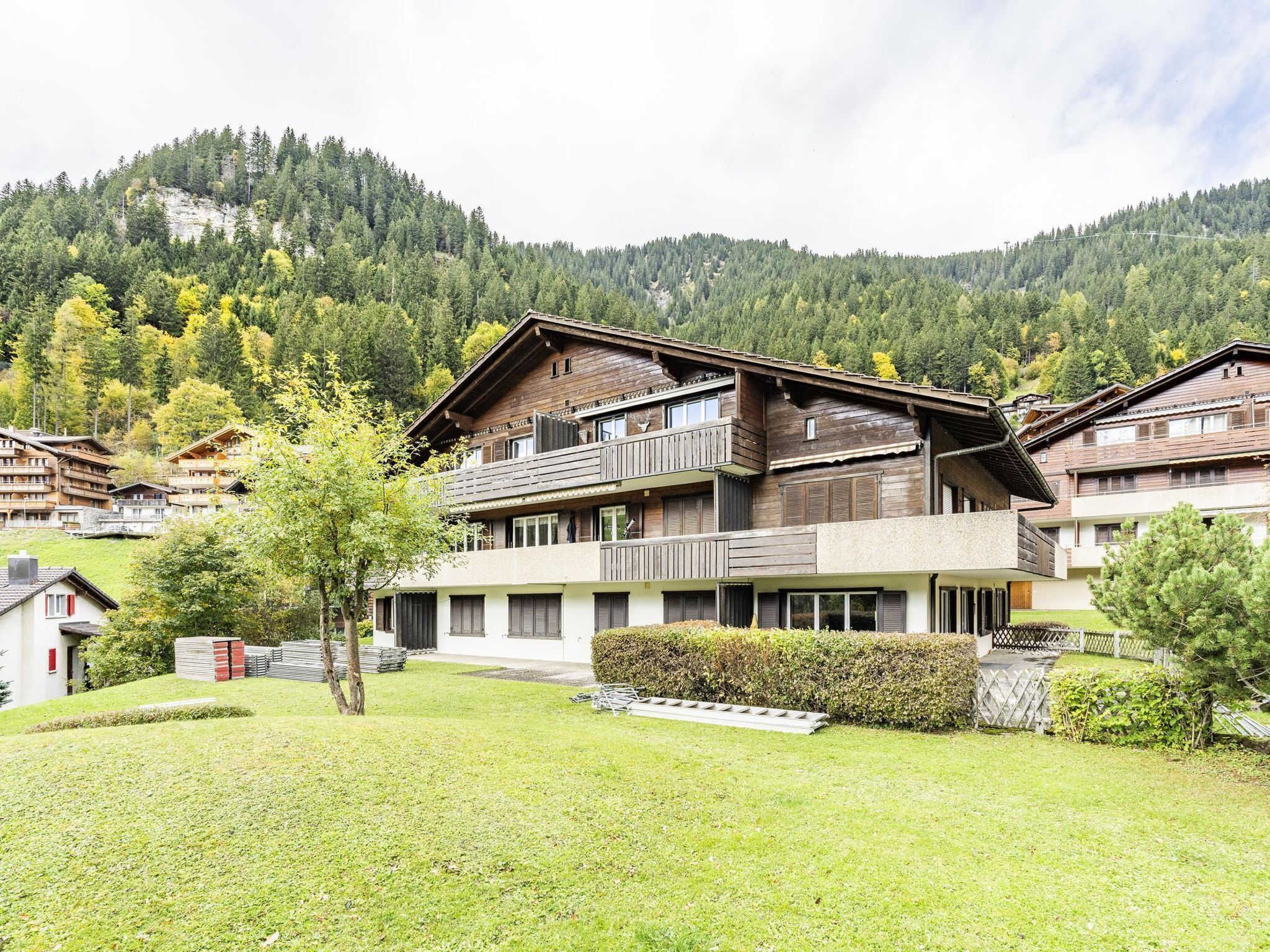 A chalet-style building with a balcony, surrounded by a well-maintained lawn and a forested mountain backdrop.